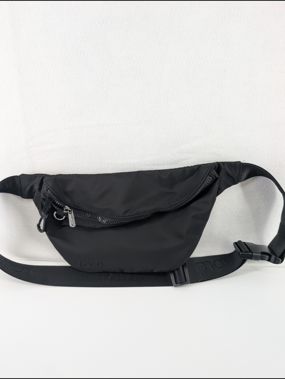 This image shows a black Lolë Taylor belt bag with an adjustable logo strap